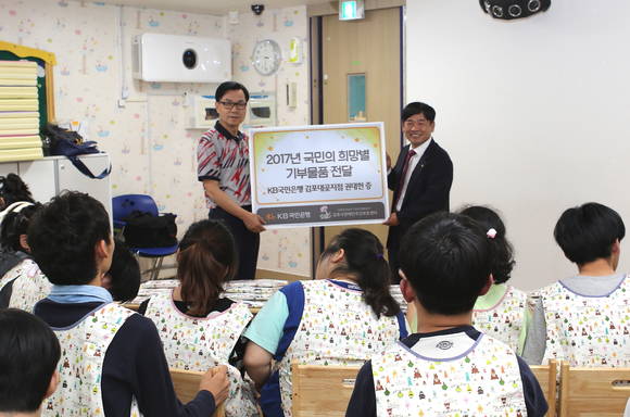 ▲'KB희망별'프로젝트 이벤트를 통해 선정된 KB국민은행 김포대곶지점 권대헌 부지점장(오른쪽)이 '김포시 장애인주간보호센터’를 방문해 앞치마를 기부하고 있는 모습.(사진제공=KB국민은행)