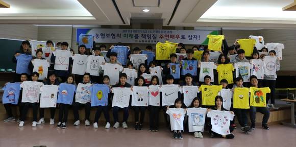 ▲ NH농협생명보험과 NH농협손해보험 신규직원들이 기후난민 어린이를 위한 손싸개와 티셔츠를 제작에 참여하고 기념 촬영을 하고 있다.(사진제공=NH농협생명)