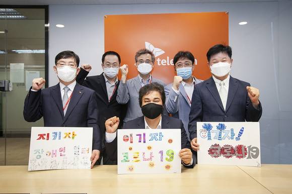▲SK텔레콤은 한국장애인고용공단과 ICT 기반의 장애인 일자리 플랫폼 구축을 위한 업무협약을 화상회의를 통해 체결했다. 유웅환 SK텔레콤 SV이노베이션센터장(앞줄 가운데) 등 체결식 참석자들이 한국장애인고용공단이 제작한 코로나19 극복 메시지를 들고 결의를 다지고 있다. / 사진=SK텔레콤