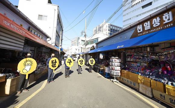 ▲대신동 양말골목 상인들이 노후간판 교체와 차양막 설치 등으로 새롭게 탈바꿈한 양말골목에서 '달구양말' 브랜드 로고와 명칭 피켓을 들고 있는 모습 / 사진=IBK기업은행