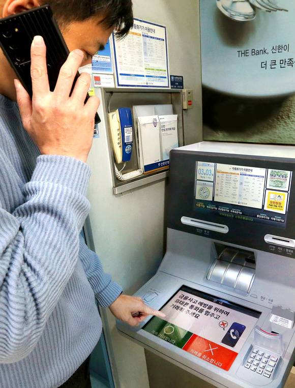 ▲휴대폰으로 통화하며 신한은행 ‘AI 이상행동탐지 ATM’을 이용하는 도중 ATM 화면에 금융사고 예방 주의 문구가 나오는 모습 / 사진=신한은행