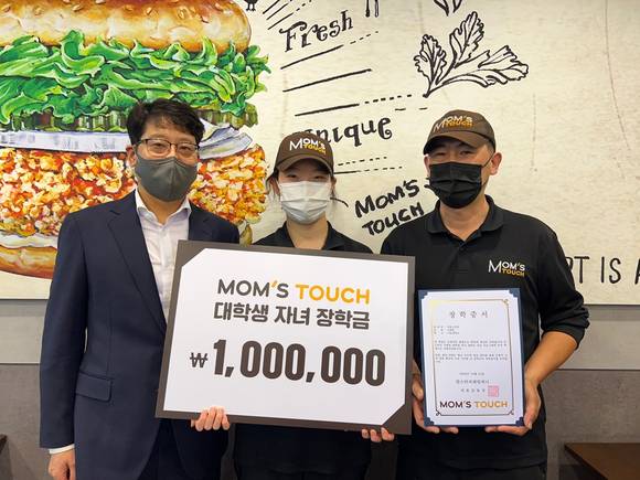 ▲김연일 맘스터치앤컴퍼니 개발운영본부장(왼쪽)과 장학금 수혜 강동고덕점 가맹점주가 기념촬영을 하고 있다. / 사진=맘스터치